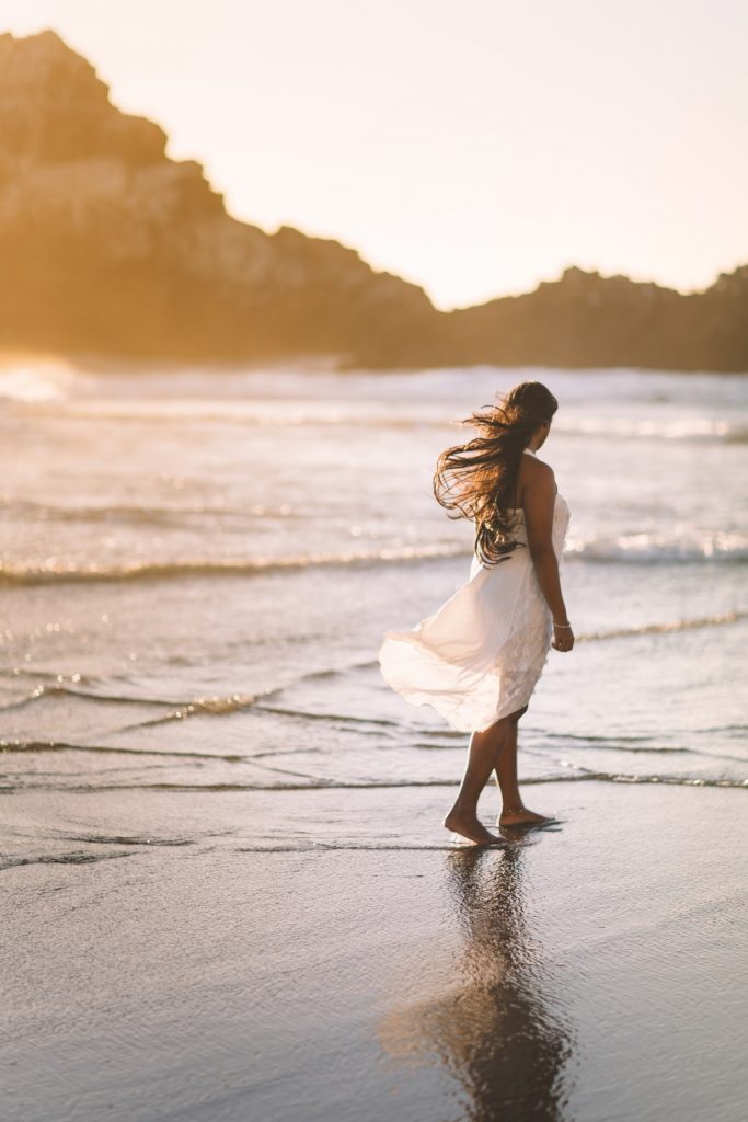 Woman walking in flowy white dress on beach