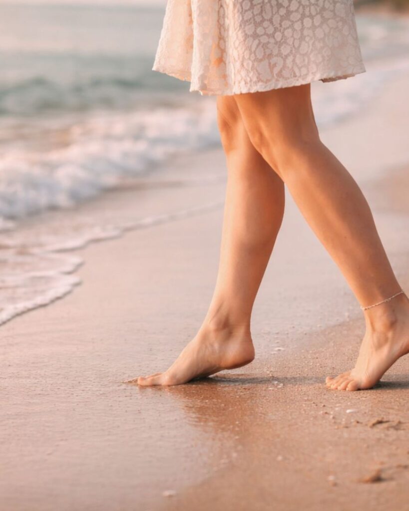 woman stepping onto sand towards the waves