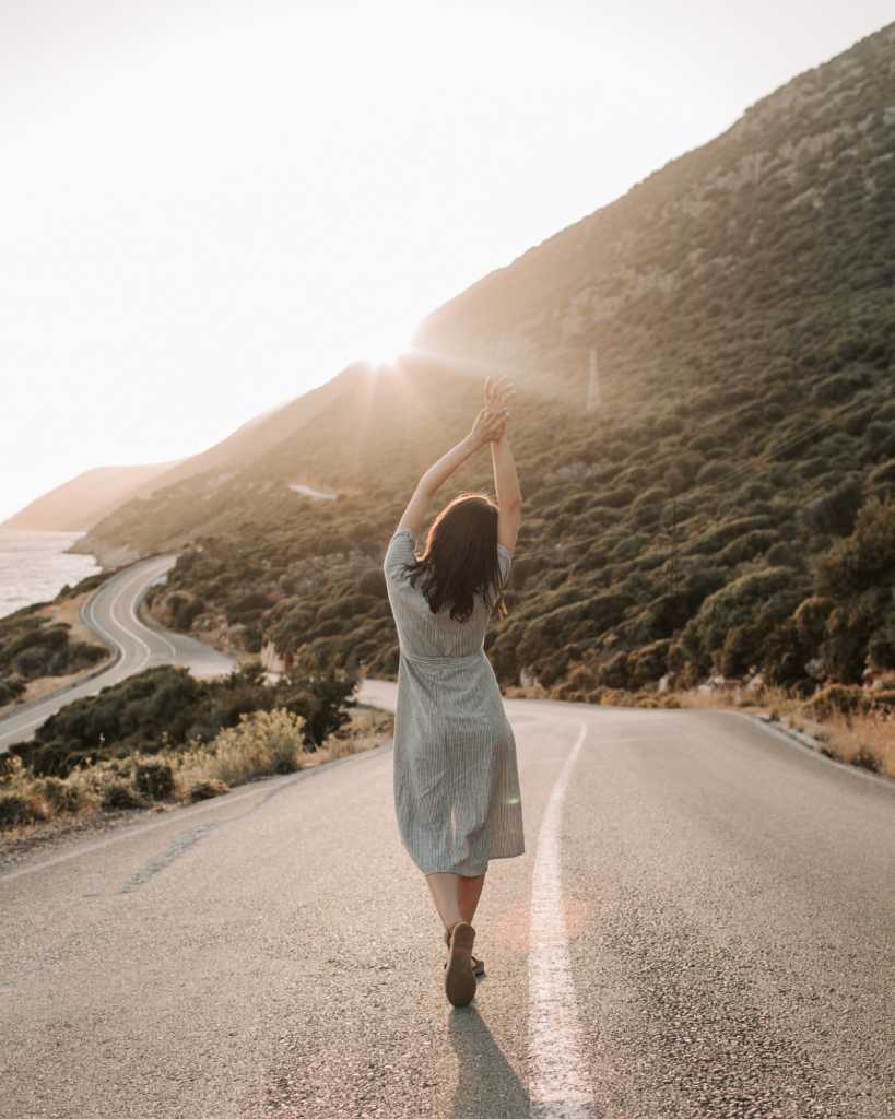 woman walking down middle of the road at sunset near a beah