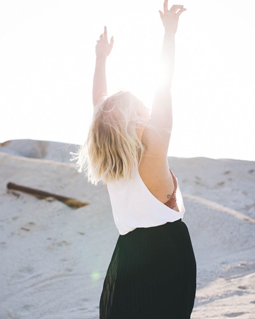 woman stretching up with both hands on the beach