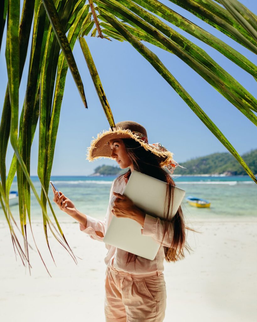 Woman in big hat under palm tree looking at her phone