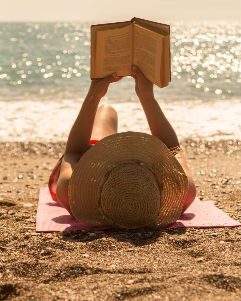Woman lays on beach reading book
